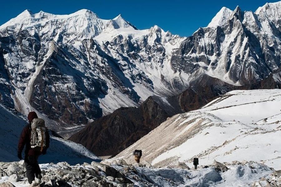 Solo trekker traversing snowy high-altitude terrain with massive Himalayan peaks towering above
